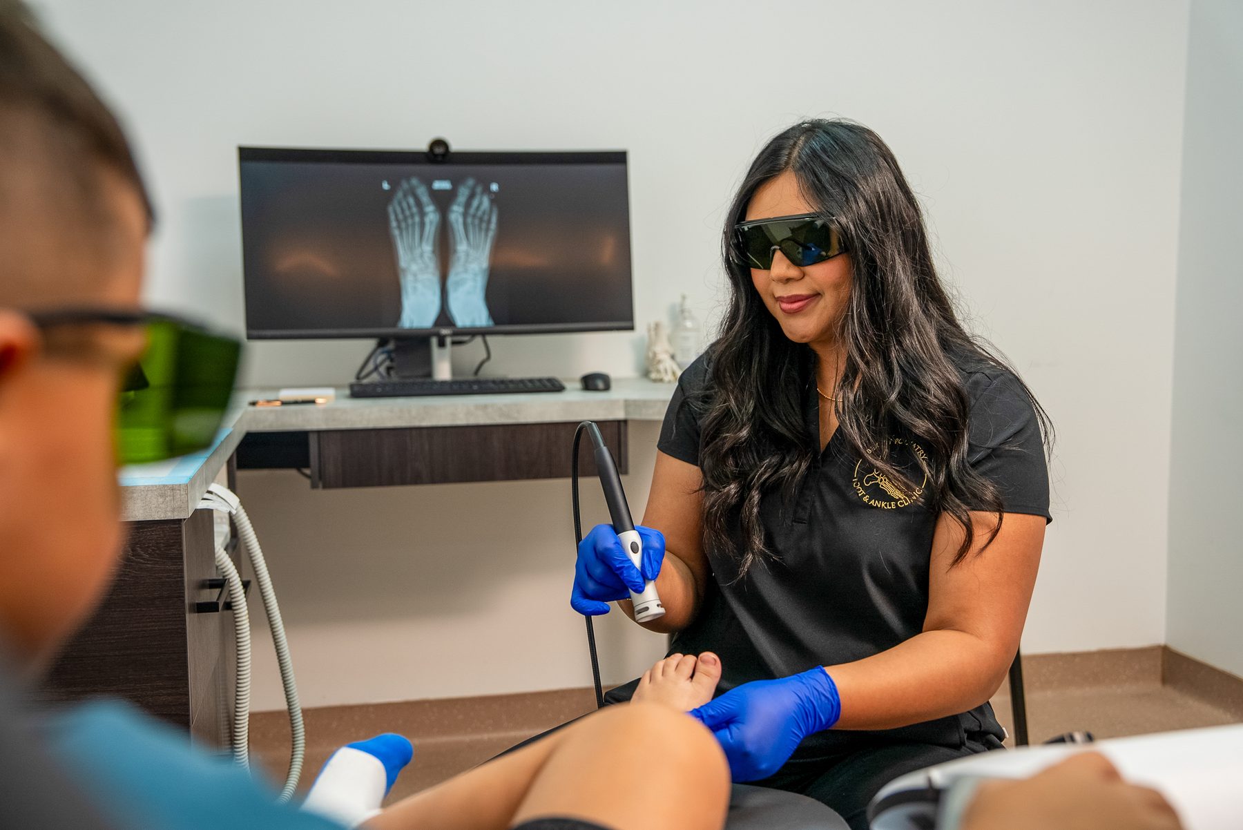 Bexley Podiatry clinician performing laser therapy with foot X-rays on screen
